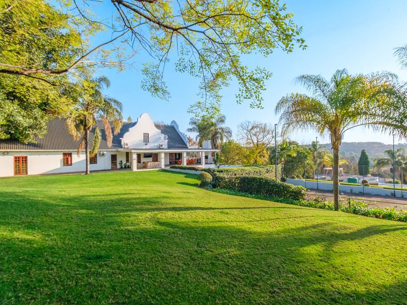 Spacious rear garden featuring a well-maintained lawn, covered patio area, and a private tennis court set against a traditional gabled house.