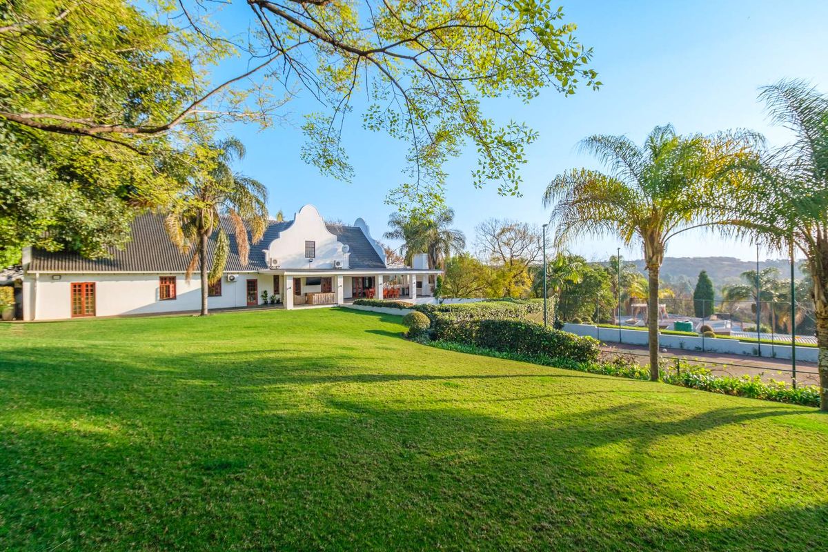 Spacious rear garden featuring a well-maintained lawn, covered patio area, and a private tennis court set against a traditional gabled house.