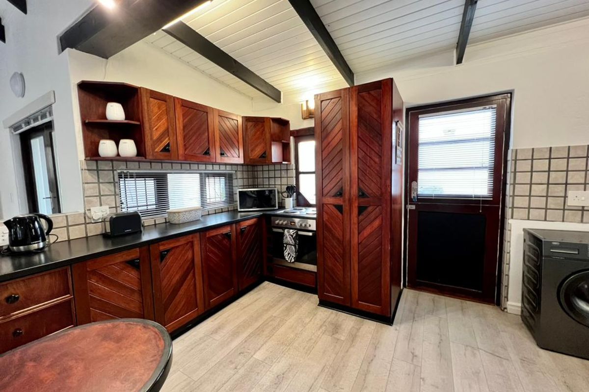 A functional kitchen featuring dark wood cabinetry, laminate countertops, tiled backsplash, and exposed ceiling beams, with direct access to an exterior door.