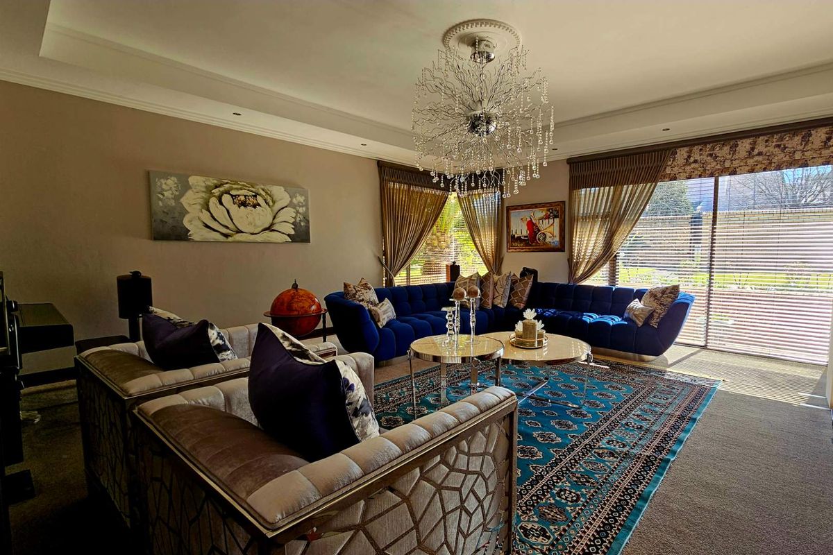 Spacious living room featuring decorative crown molding, a statement crystal chandelier, and large windows with integrated blinds providing natural light.
