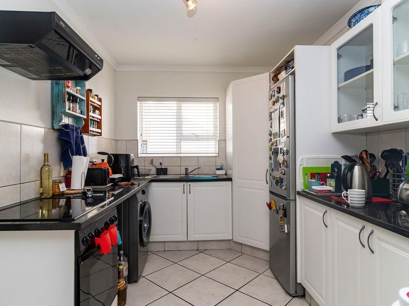 A functional kitchen featuring white cabinetry, dark countertops, tiled backsplash, built-in oven with extractor fan, and tiled flooring.