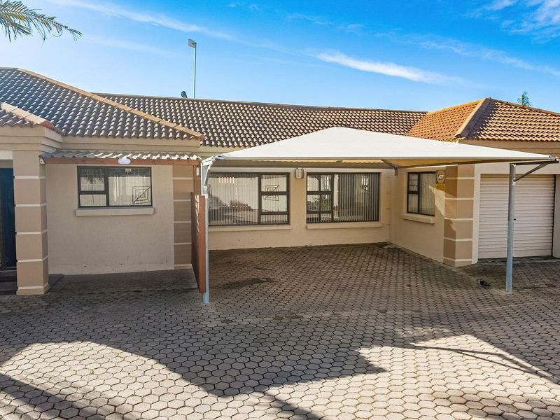 Front elevation of a townhouse featuring a paved driveway, shade sail carport, and double garage with tiled roofing.