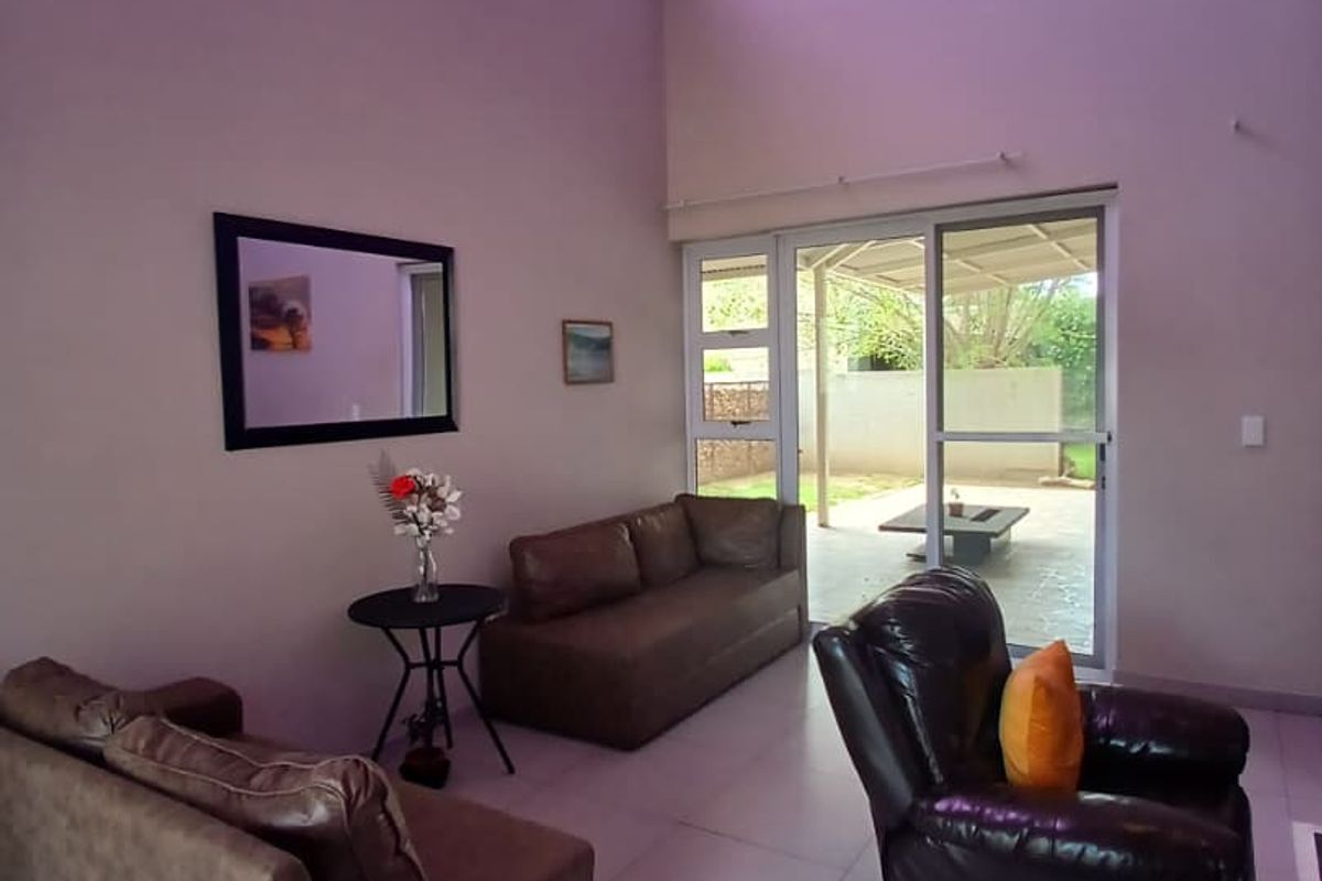 Spacious living room featuring high vaulted ceilings, large skylight, and tiled flooring, with direct access to an outdoor patio area through sliding glass doors.