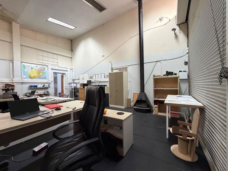 Spacious office area featuring high ceilings, a freestanding fireplace, and a secure roller shutter door, providing a functional workspace with industrial character.