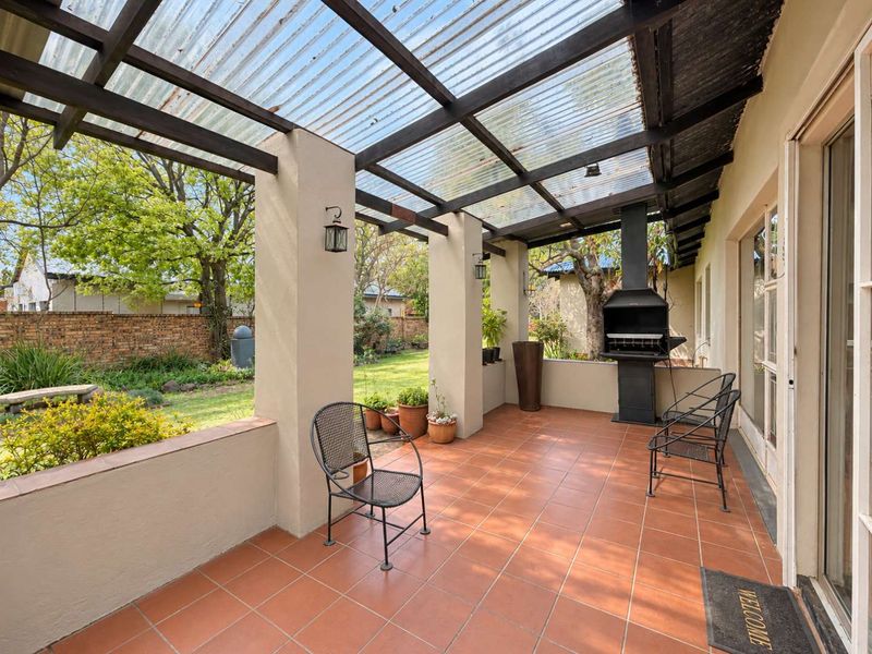 Covered patio featuring terracotta tiling, a built-in braai, and a timber pergola structure with a corrugated roof, overlooking the garden.