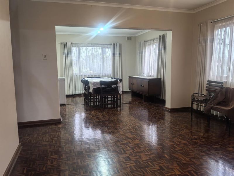 Spacious open-plan living and dining area featuring classic parquet flooring, neutral walls, and large windows providing ample natural light.