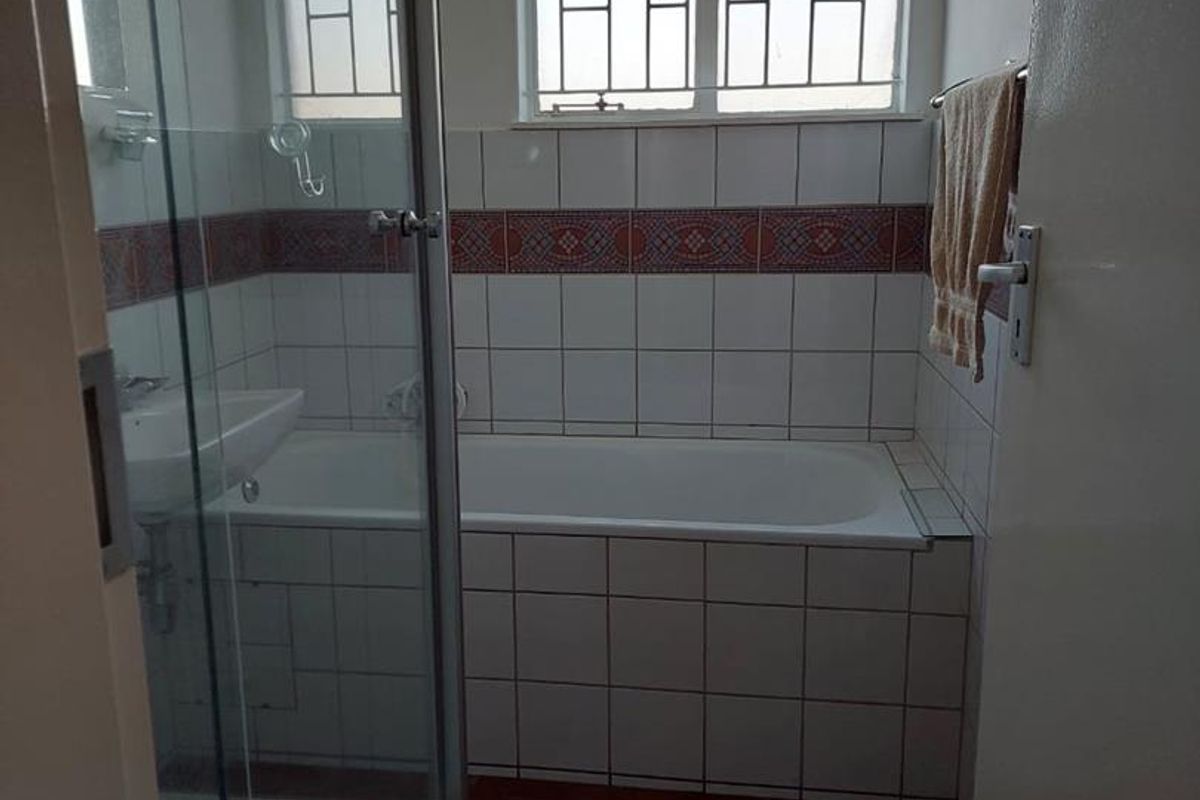 A functional bathroom featuring a built-in bathtub, a separate glass-enclosed shower, and tiled flooring with decorative wall accents.