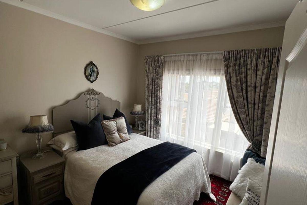 A cozy bedroom featuring tiled flooring, a central ceiling light fixture, and a window with curtain tracks.