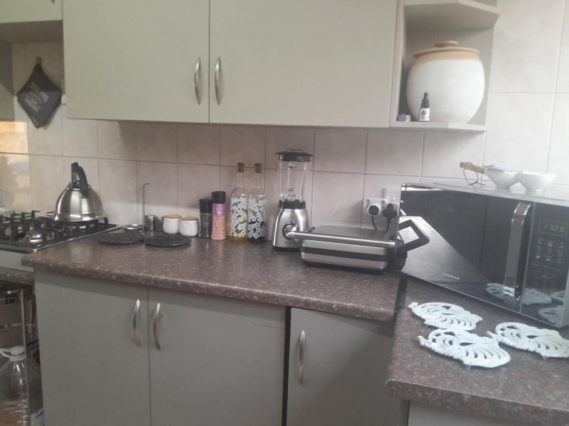 A functional kitchen area featuring laminate countertops, built-in cabinetry, and a gas hob with a tiled backsplash.