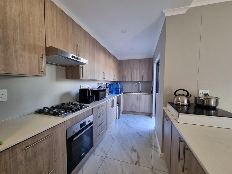 Modern galley-style kitchen featuring wood-grain cabinetry, stone countertops, gas hob, built-in oven, and elegant marble-look floor tiles.