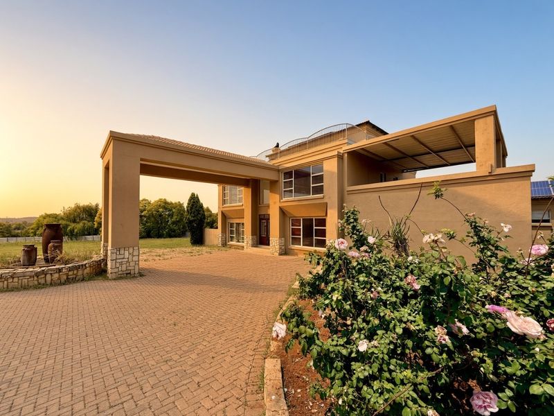 A grand front elevation featuring a paved driveway, a prominent porte-cochere, and a spacious upper-level balcony with stone-clad architectural details.