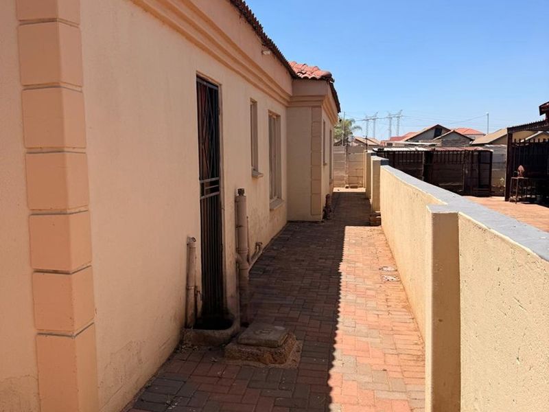 A side exterior view of the property featuring a paved walkway, boundary wall, and external plumbing fixtures along the building facade.