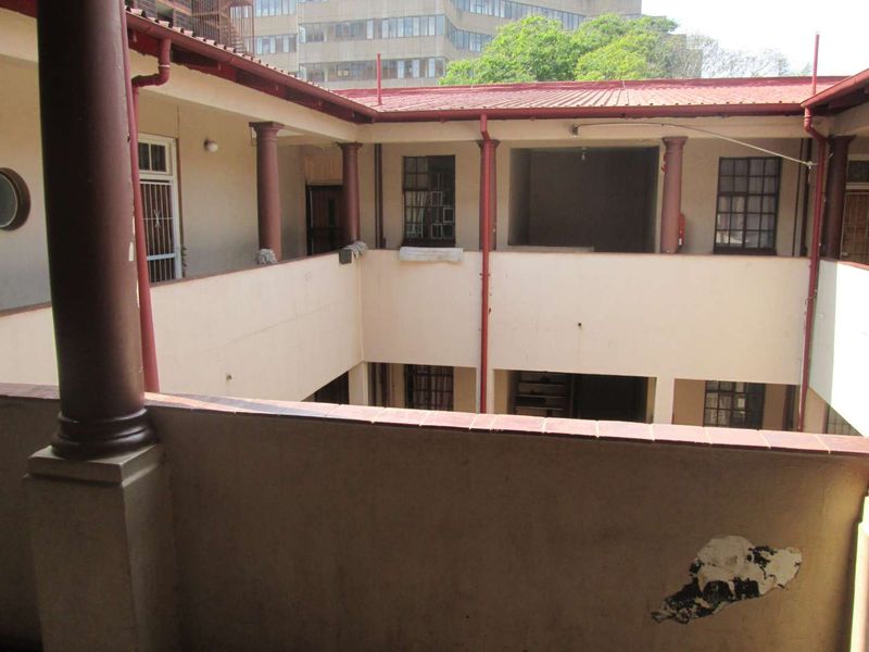 An open-air central courtyard area of an apartment complex featuring covered walkways, structural columns, and metal-framed windows.