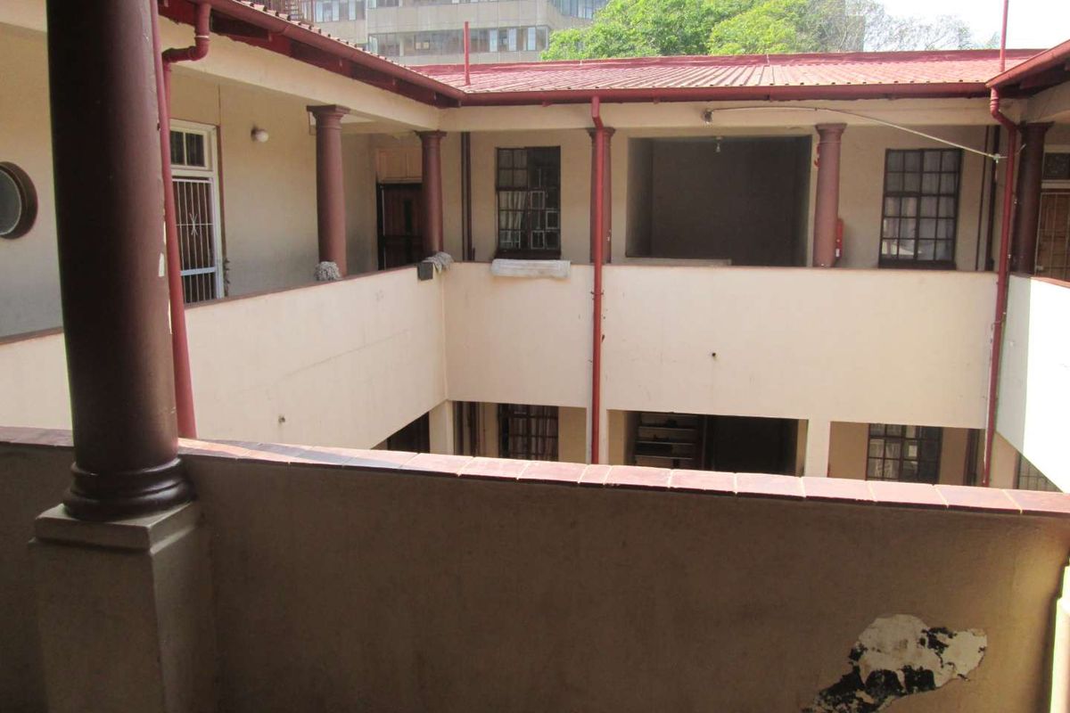 An open-air central courtyard area of an apartment complex featuring covered walkways, structural columns, and metal-framed windows.