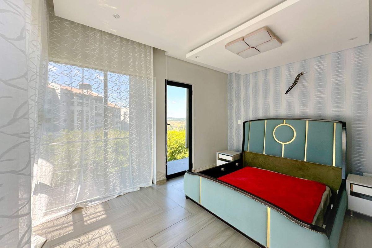 A bright and modern bedroom featuring tiled flooring, a recessed ceiling with integrated lighting, and direct access to an outdoor balcony.