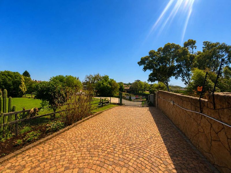 A well-maintained entrance to the small holding featuring a cobblestone driveway, stone boundary wall, and secure metal gate leading into the property.
