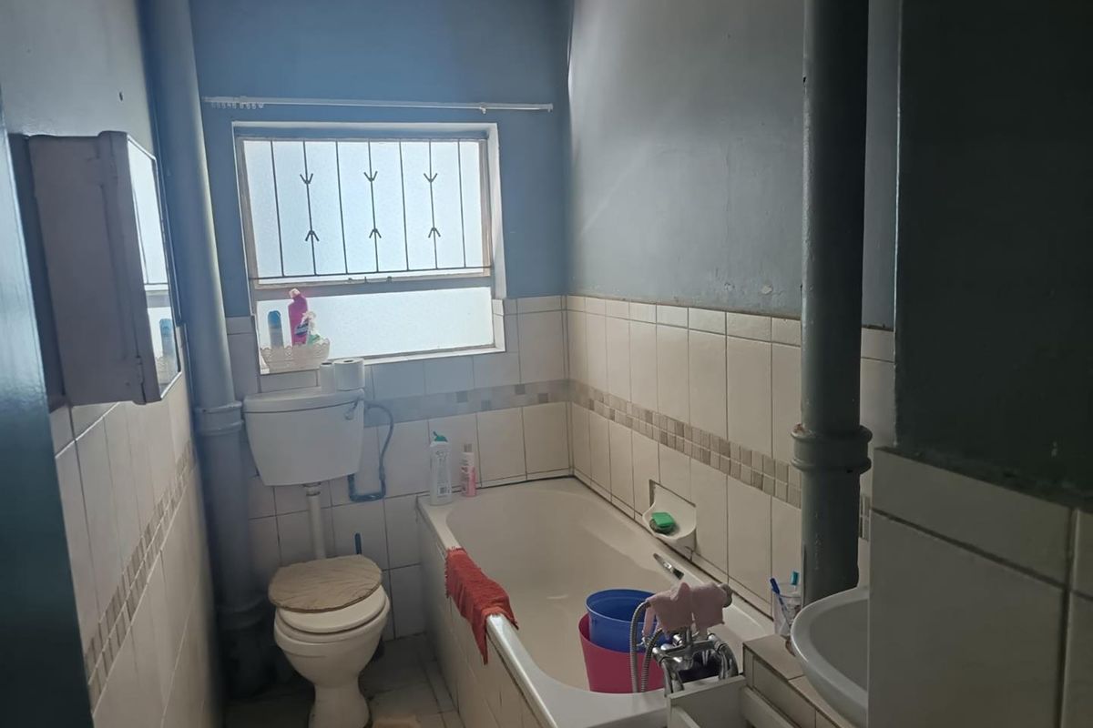 A functional bathroom featuring a bathtub, toilet, and washbasin with tiled walls and security bars on the window.