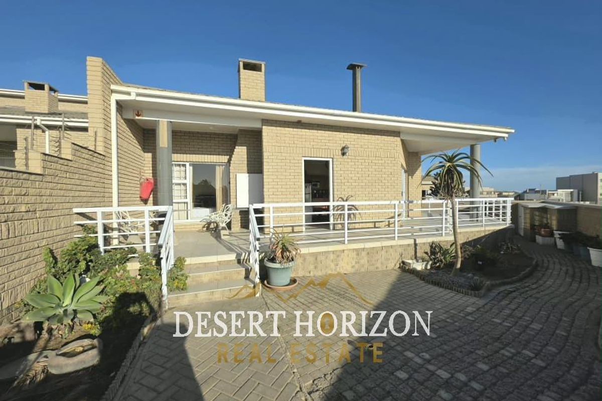 A rear exterior view of the apartment featuring a paved patio area, brick facade, and a covered veranda with metal railings.