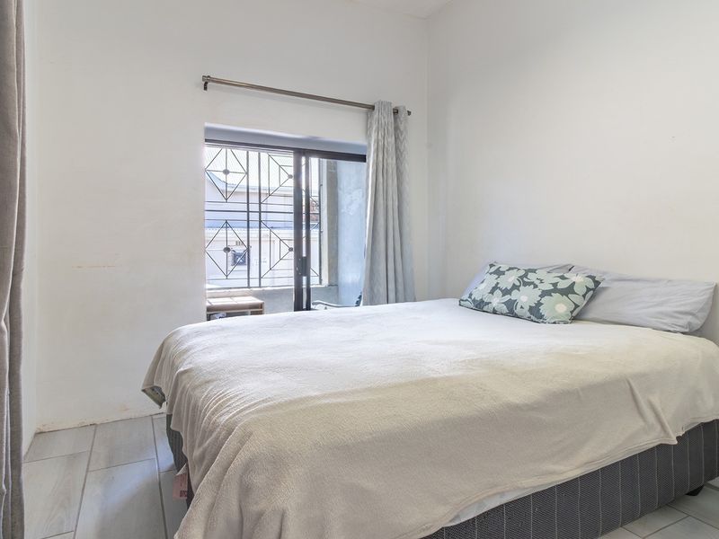 A functional bedroom featuring tiled flooring, a built-in cupboard, and a sliding door with a security gate leading to an outdoor area.