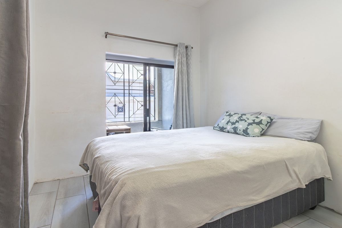 A functional bedroom featuring tiled flooring, a built-in cupboard, and a sliding door with a security gate leading to an outdoor area.