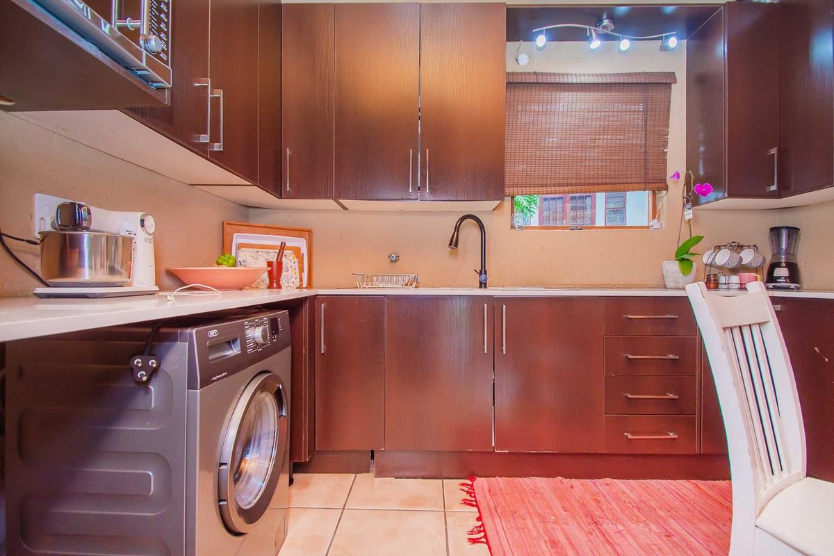 Compact kitchen featuring dark wood-finish cabinetry, integrated washing machine space, modern faucet, and tiled flooring with ample storage.
