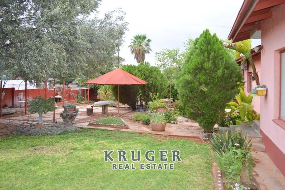 A rear garden area featuring a paved patio space, established trees, and lawn, accessible from the side of the house.