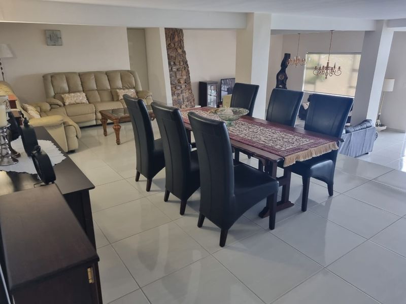 Spacious open-plan living and dining area featuring large format floor tiles, a decorative stone feature wall, and integrated lighting.