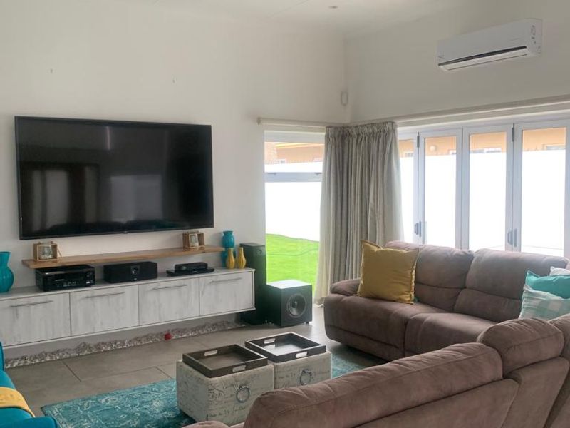 A bright and spacious living room featuring tiled flooring, recessed downlights, a wall-mounted air conditioner, and bi-fold doors leading to the garden.