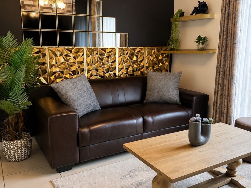 A well-maintained living room featuring tiled flooring and a striking decorative gold-toned wall feature, creating a modern and sophisticated atmosphere.