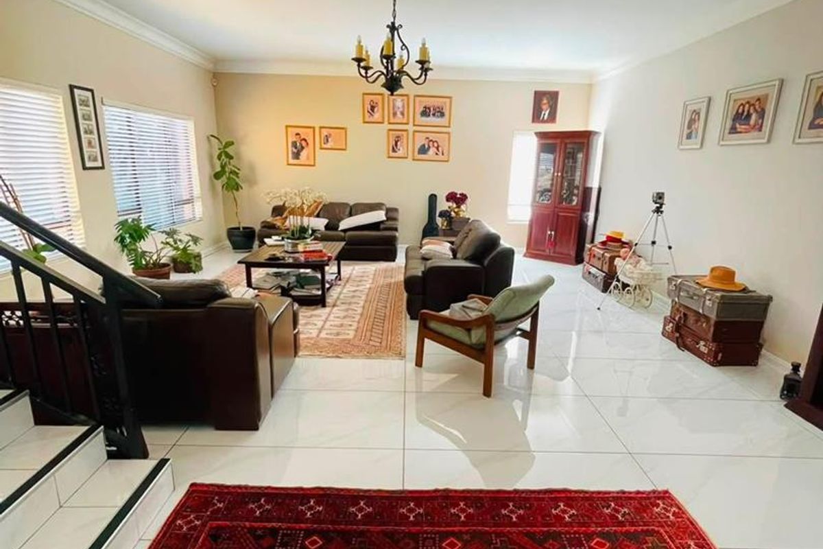 Spacious living room featuring polished white floor tiles, a decorative chandelier, and a staircase with a modern metal railing.