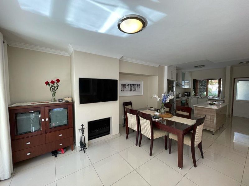Open-plan living and dining area featuring a built-in fireplace, tiled flooring, and a modern kitchen with a central island.