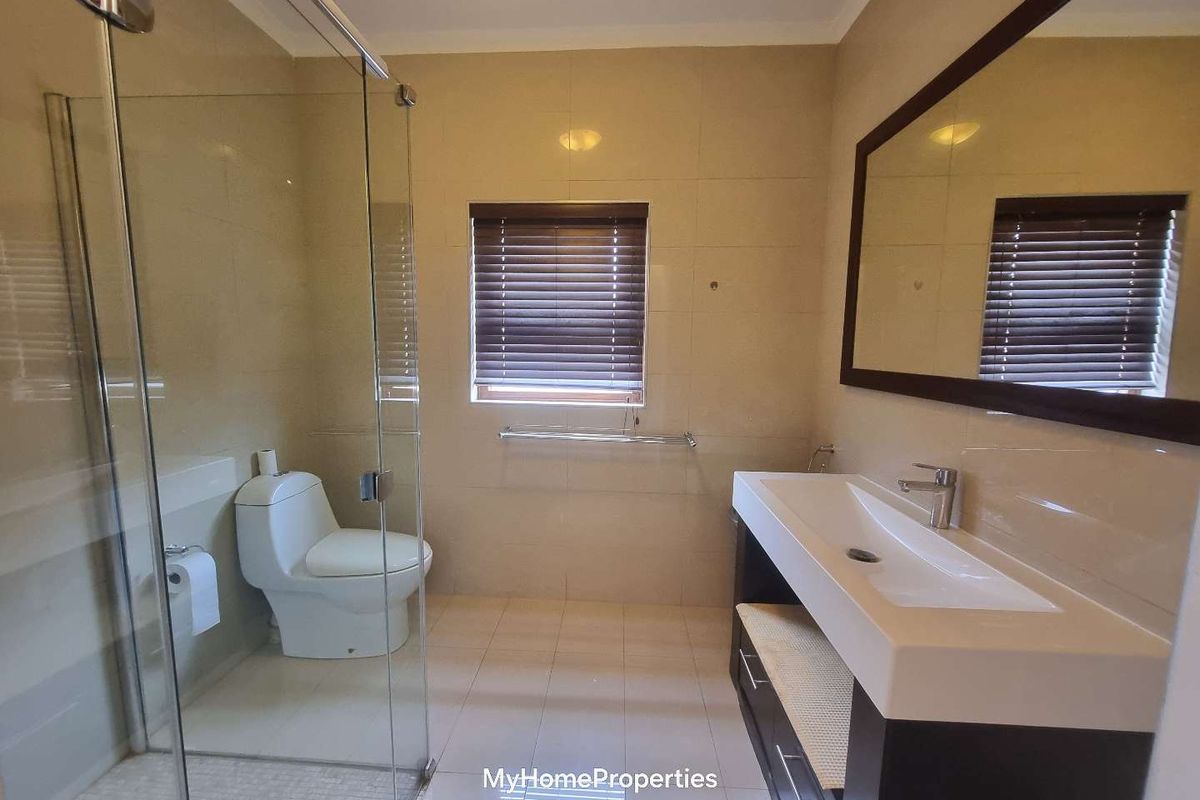 A clean, modern bathroom featuring a glass-enclosed shower, a vanity with a basin, and neutral wall and floor tiling.