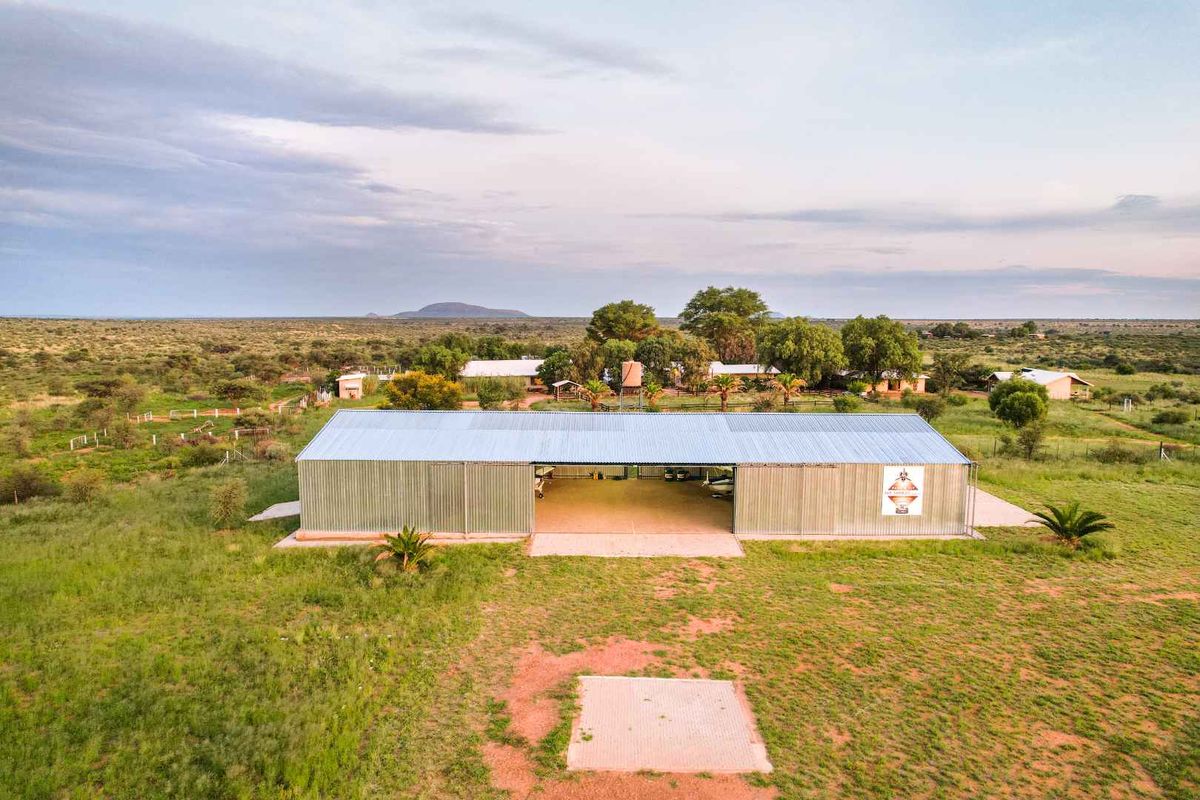 Aerial view of a large metal-clad hangar or utility building situated on a rural farm property with surrounding landscape.
