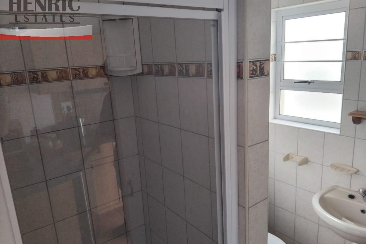 A functional bathroom featuring a glass-enclosed shower, wall-mounted basin, and a window providing natural light.