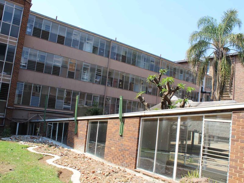 Rear view of an apartment building featuring brick exterior walls, extensive louvre window installations, and a ground-level garden area with paved access.