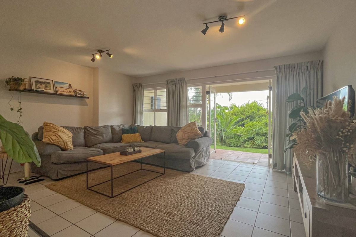 A bright living room featuring tiled flooring, track lighting, and large glass doors opening onto a private garden patio.