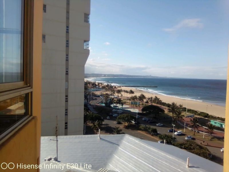 Elevated coastal view overlooking the beach, promenade, and surrounding urban landscape from an apartment window.