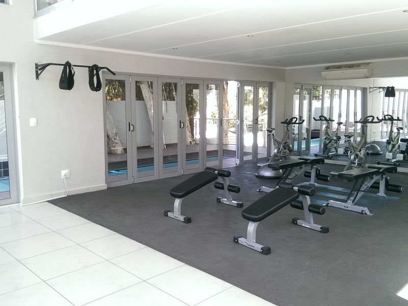 A spacious, well-lit gym area featuring rubber flooring, full-length mirrors, and large aluminium stackable doors providing direct access to the pool area.