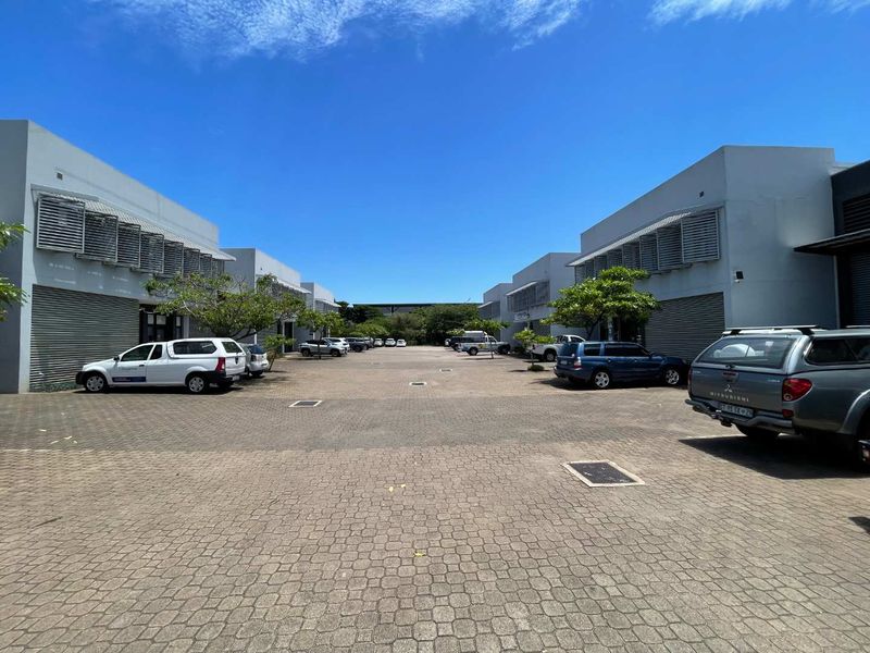 A paved commercial courtyard area featuring multiple units with roller shutter doors and fixed louvred window awnings, providing ample exterior parking space.