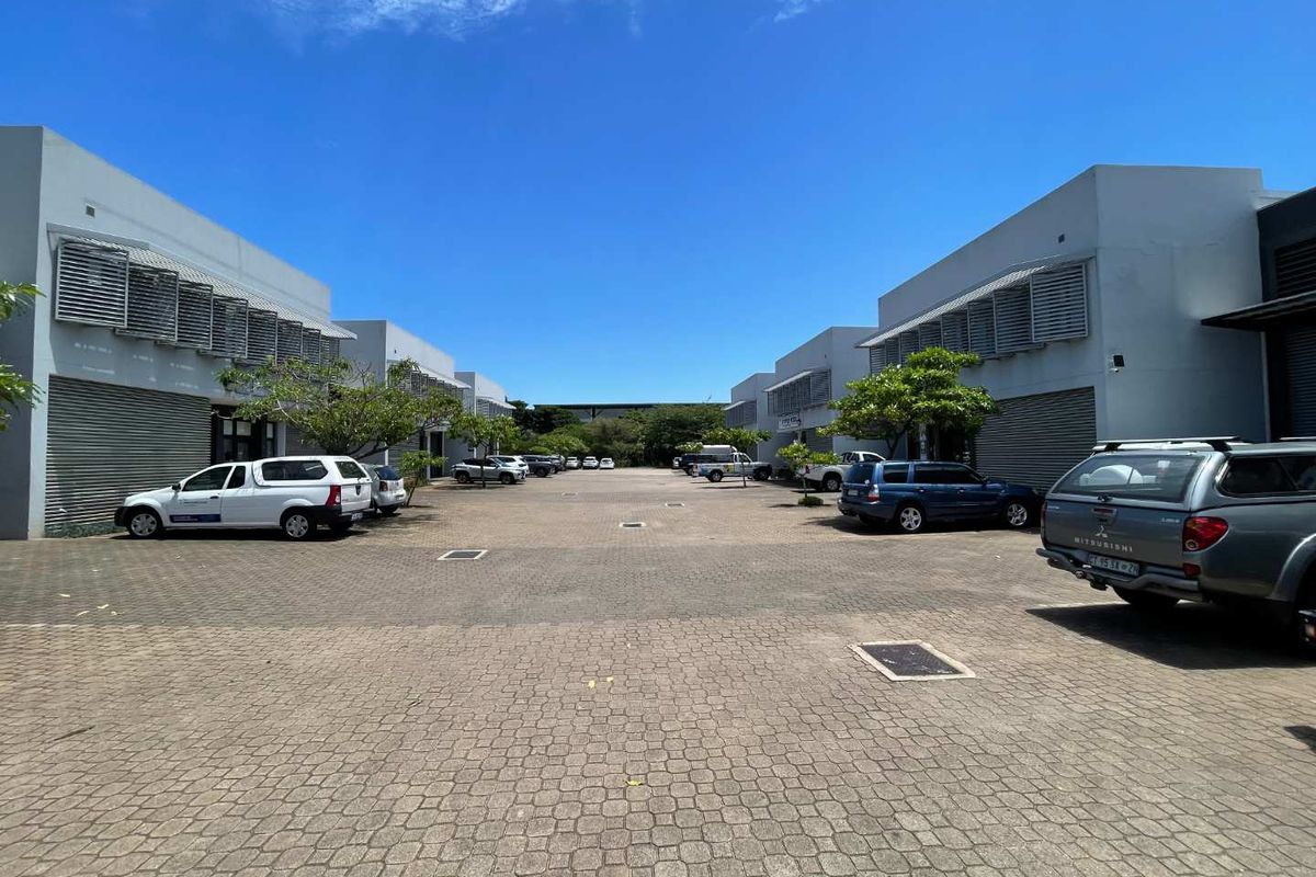 A paved commercial courtyard area featuring multiple units with roller shutter doors and fixed louvred window awnings, providing ample exterior parking space.