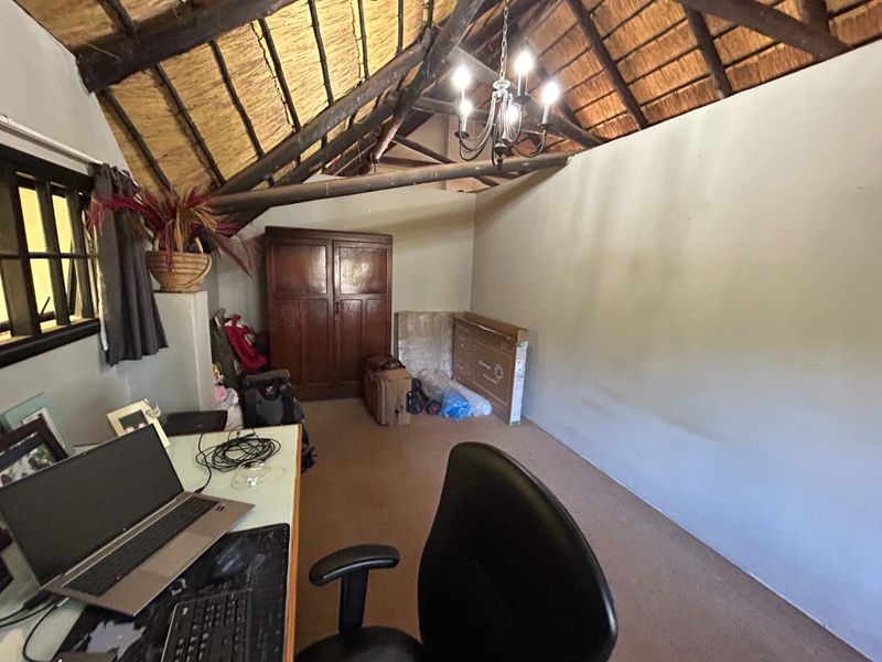 A bedroom featuring a high-pitched thatched roof with exposed timber rafters, a central chandelier, and a built-in wooden cupboard.