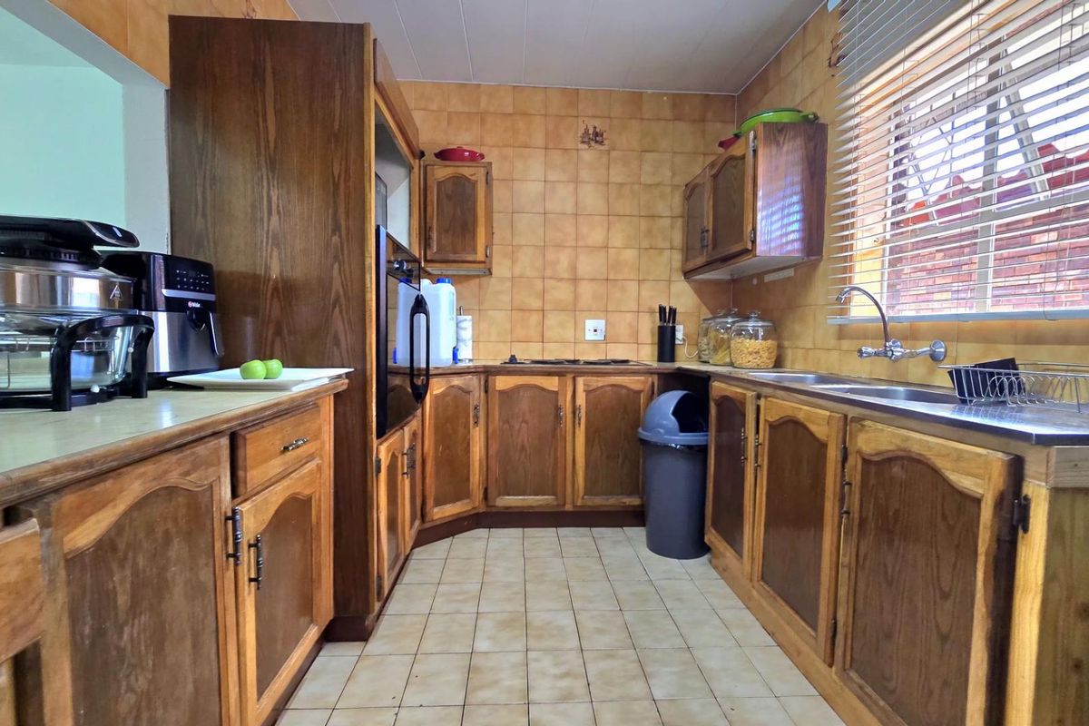 A functional kitchen featuring traditional wooden cabinetry, tiled backsplash, and tiled flooring, offering a classic layout with ample storage and preparation space.