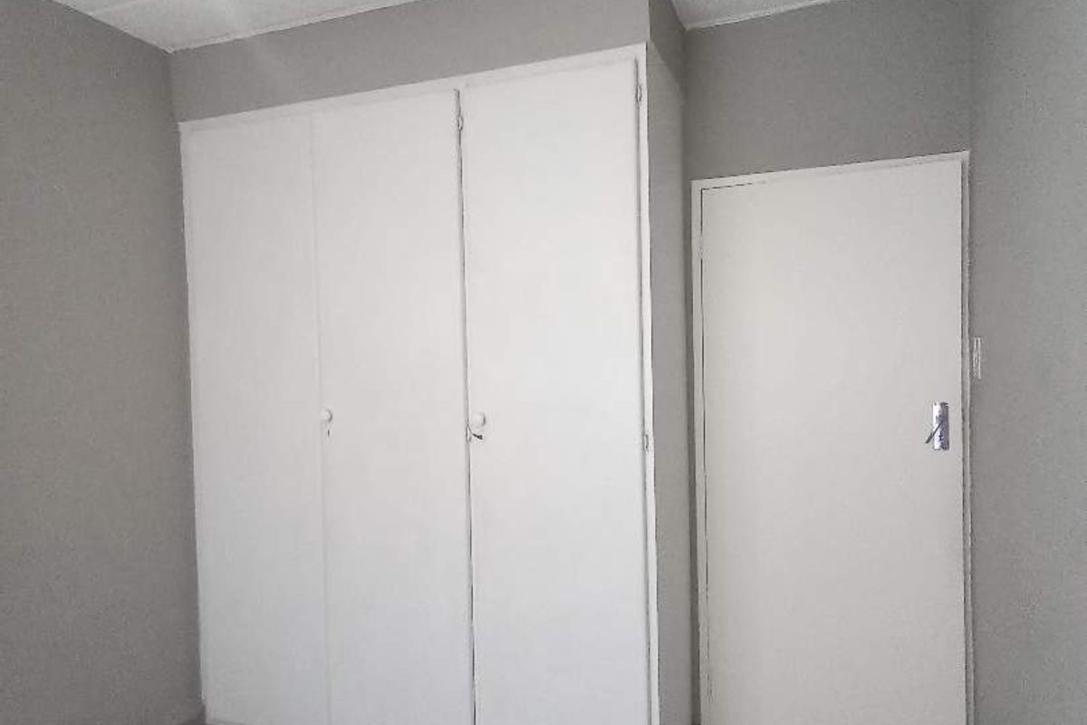 A simple, empty bedroom featuring neutral grey walls, tiled flooring, and a built-in wardrobe, offering a clean canvas for personalization.