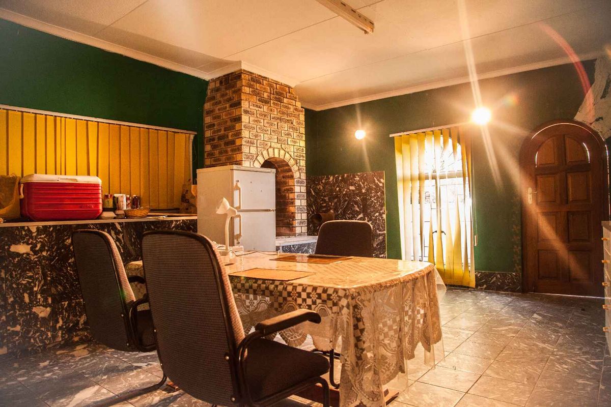 A living area featuring a prominent brick fireplace, tiled flooring, and dark green wall finishes with vertical blinds.