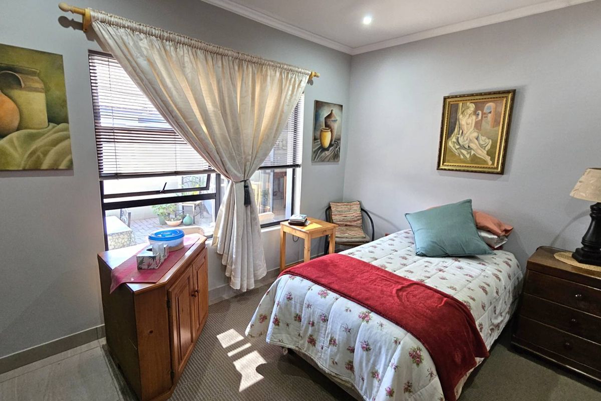 A cozy bedroom featuring neutral wall tones, carpeted flooring, and a large window that allows for natural light.