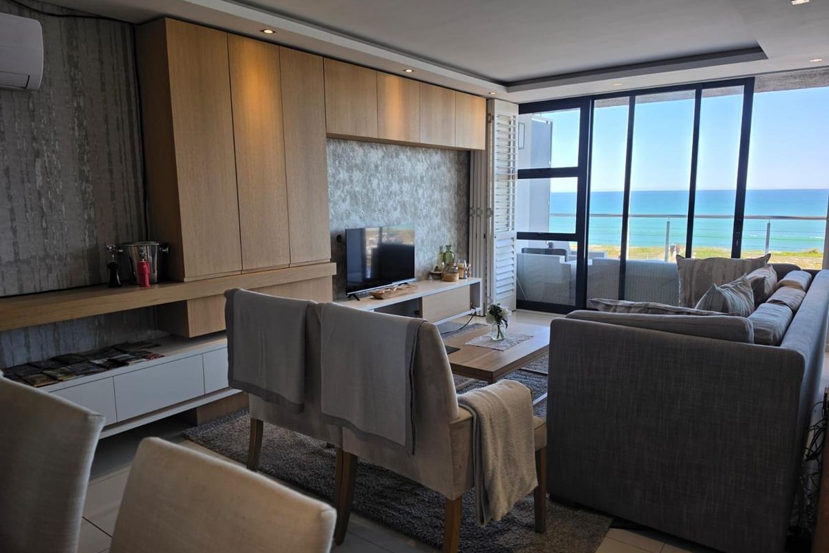 Modern living room featuring custom built-in cabinetry, recessed lighting, and large sliding glass doors opening to a balcony with ocean views.