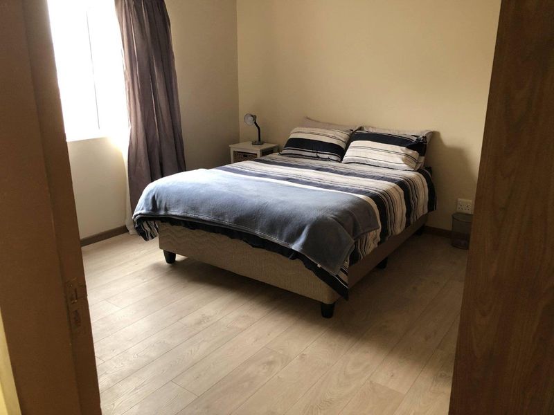 A functional bedroom featuring light-toned laminate flooring and a window, providing a neutral base for personal styling.
