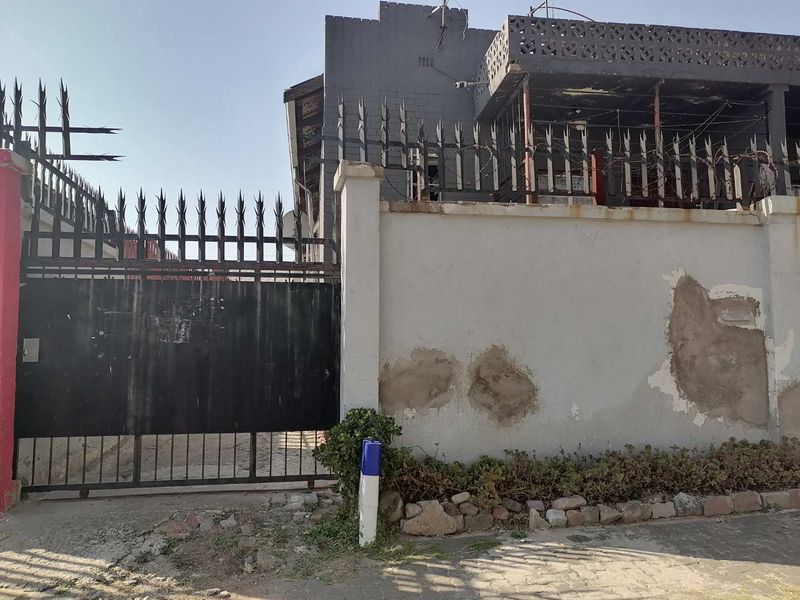 Front exterior view of the property featuring a metal security gate, perimeter wall with visible plaster damage, and an upper-level balcony.