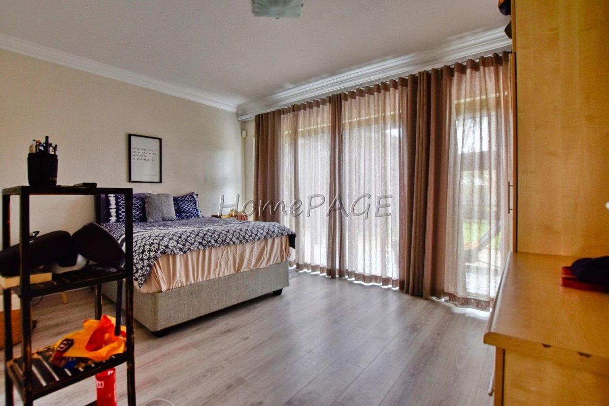 A spacious bedroom featuring light wood-look flooring, crown molding, and large sliding glass doors with floor-to-ceiling curtains providing access to the outdoors.
