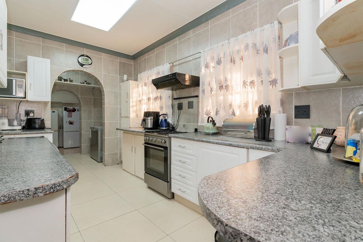 A functional kitchen featuring granite-look countertops, built-in cabinetry, a stainless steel oven with extractor fan, and an arched entryway leading to a scullery area.